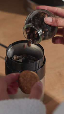 mujer vierte granos de café en el molinillo en la mesa de primer plano. señora pone granos tostados en la máquina en casa. aparato para bebidas con cafeína haciendo en la cocina