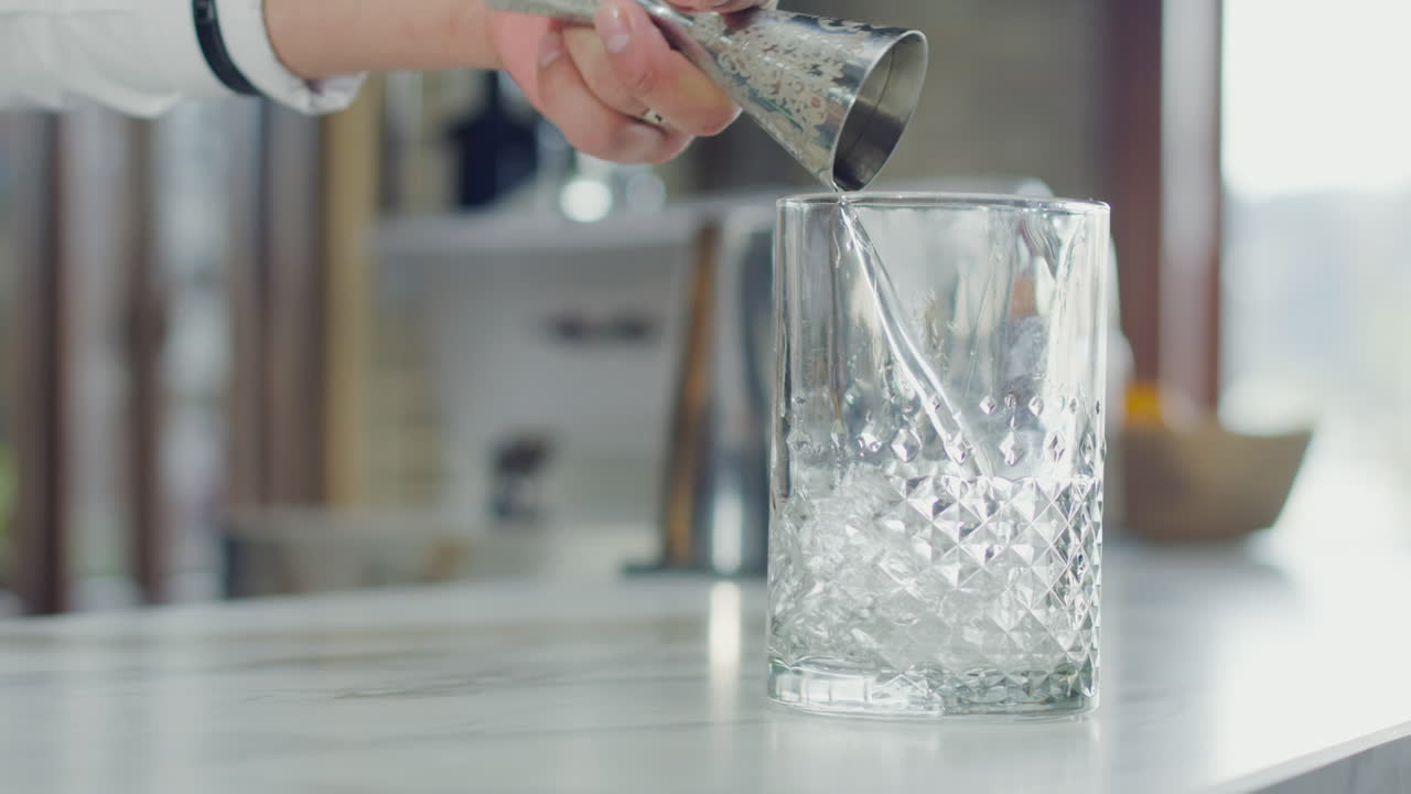Close-up of a bartender pouring liquor from a jigger into a glass