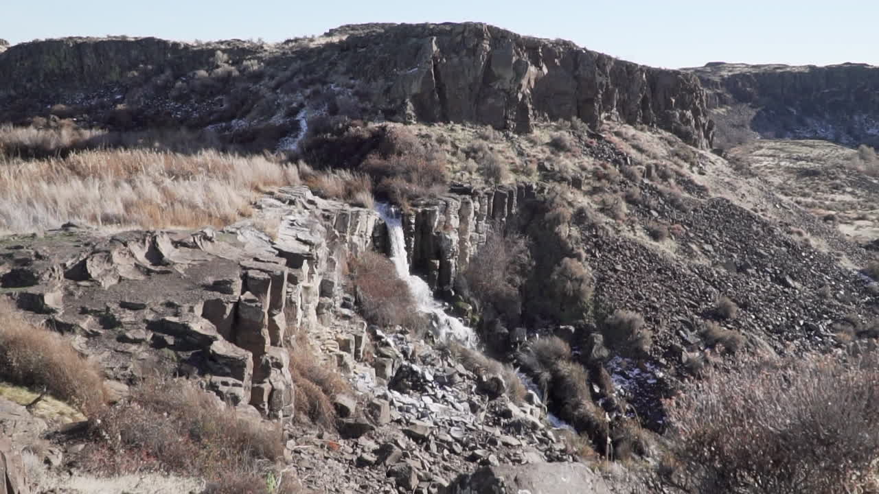 Zooming in wide shot of a waterfall, surrounded by rocks and bushes
