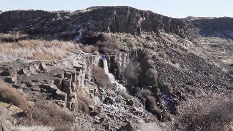 zooming in wide shot of a waterfall, surrounded by rocks and bushes