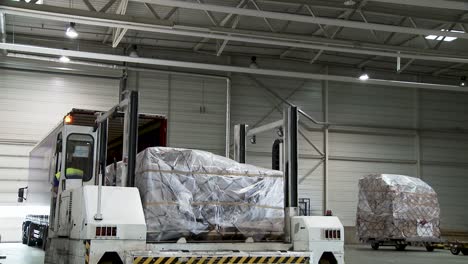 Worker-unloads-truck-at-modern-international-warehouse-with-big-fork-lift-vehicle