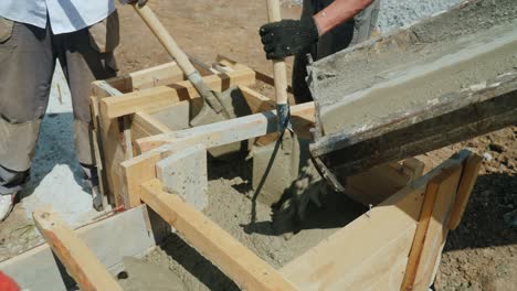 trabajar con hormigón en el sitio de construcción. los trabajadores llevan hormigón a un molde de madera. trabajo manual pesado en el lugar de construcción