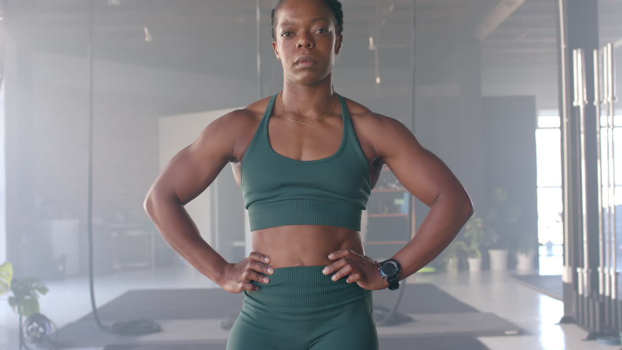 Confident woman in gym wearing fitness attire, standing with hands on hips