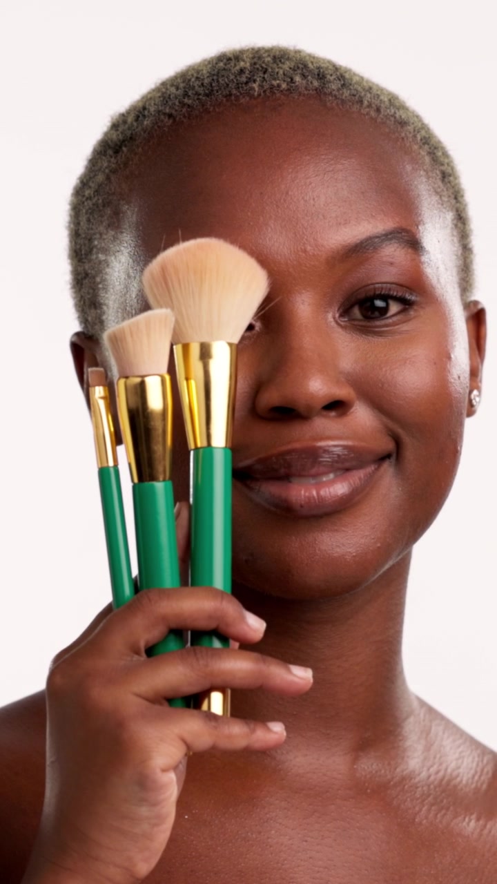 Young Woman Holding Makeup Brushes and Smiling at Camera