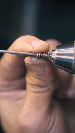 cu: skilled jeweler uses special tool to coil thin gold cable on blurred background in workshop extreme close view