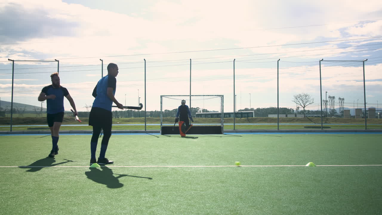 Playing field hockey, men practicing drills on outdoor field with goalie