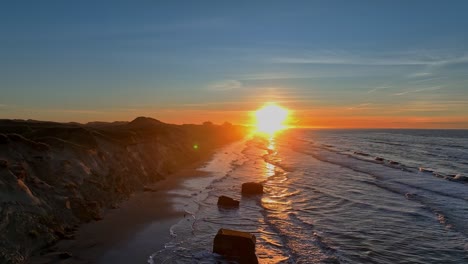 sea waves are washing on the beach, high dunes have formed, the remains of war bunkers are on the beach, and the sun is setting on a winter evening