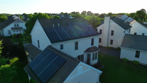 aerial rotation around solar panels on rooftop of residential home. green foliage and sunset in a beautiful small town in america. clean energy theme with sun flare