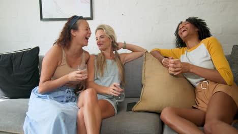 diverse female friends relaxing on sofa, enjoying drinks and conversation at home