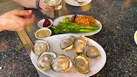 hands preparing oysters with condiments and greens