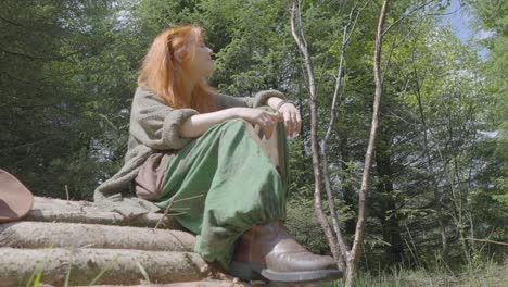 chica sentada en una pila de troncos al sol en el bosque en verano a media velocidad cámara lenta