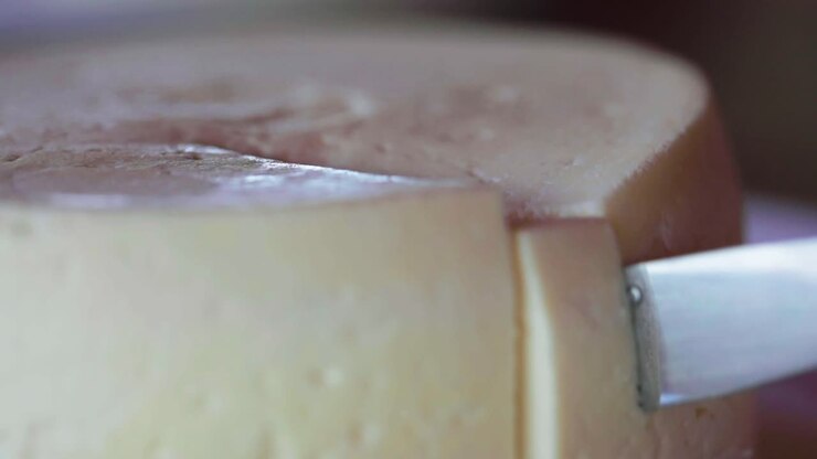 Knife cutting round cheese wheel, closeup shot