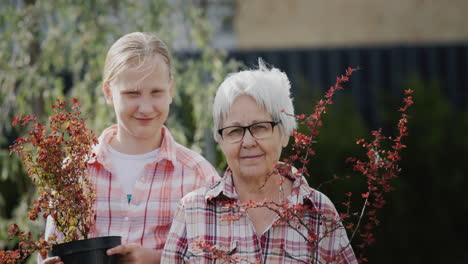 Portrait-of-an-elderly-woman-with-her-granddaughter-holding-potted-plants-for-planting-in-the-garden