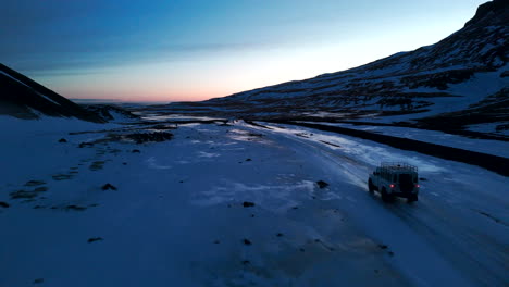 tracking shot of white jeep riding through vast snowy iceland landscape during dusk