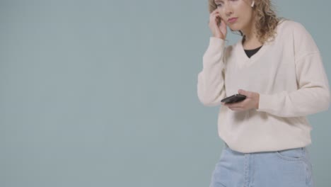 Close-Up-Shot-Of-Young-Woman-Listening-To-Music-On-Mobile-Phone-And-Dancing-Against-Blue-Background