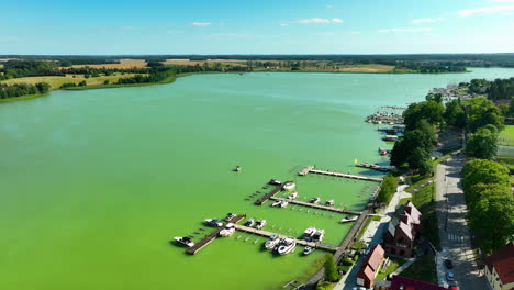 aerial shot of the green lake and marina in ryn, warmia-masuria, with boats and surrounding countryside, highlighting the serene water and scenic views