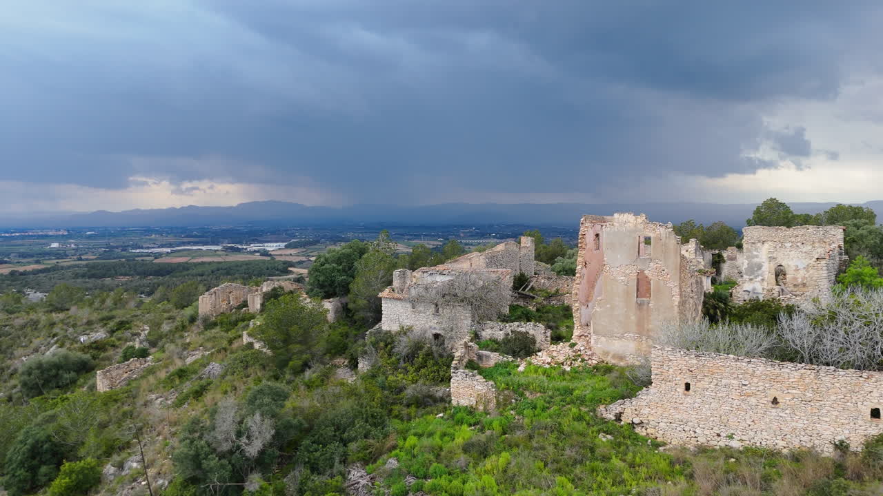 Drone flies above ancient stone ruins as the camera tilts up to reveal distant mountains and dramatic storm clouds in the sky