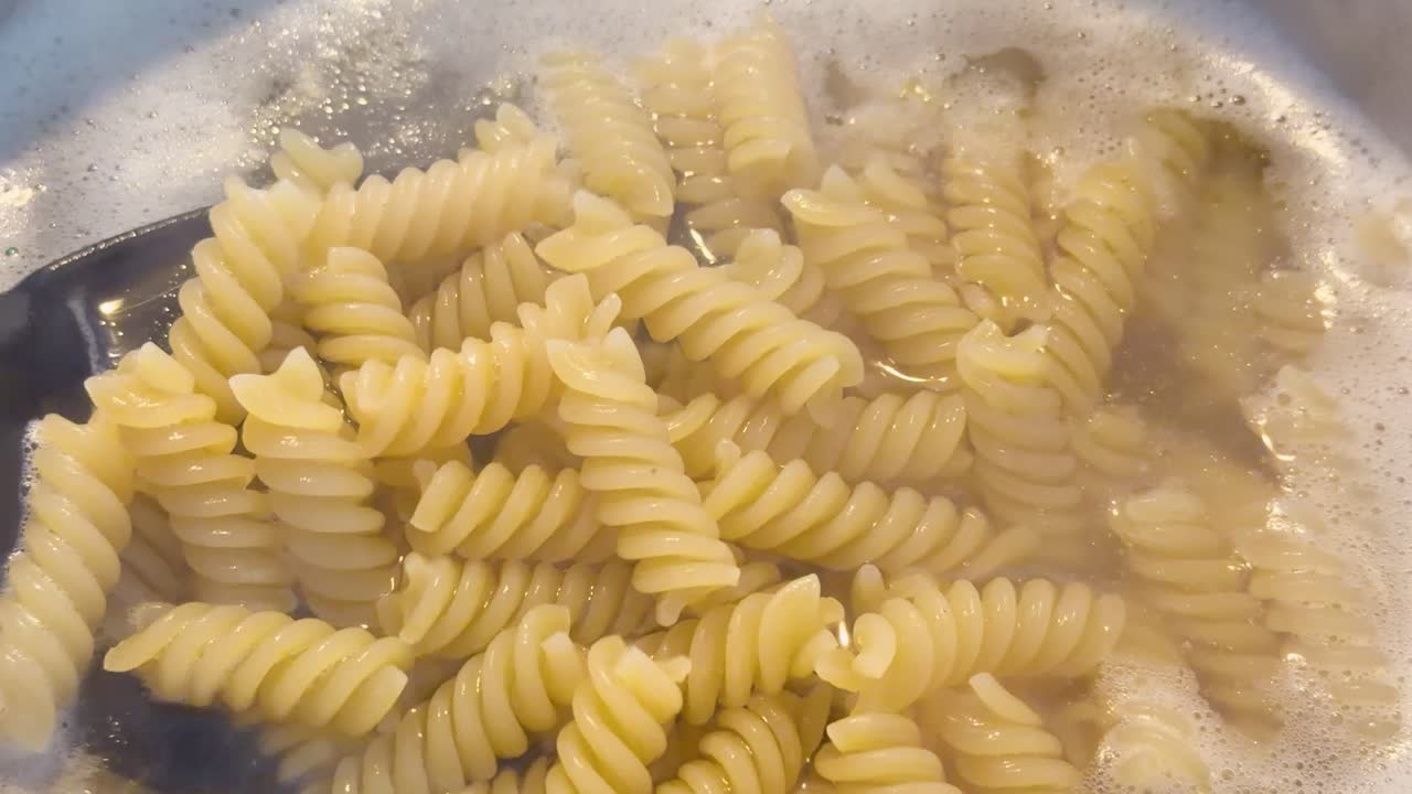 Close-up shot of fusilli pasta boiling in bubbling water on an induction hob with steam