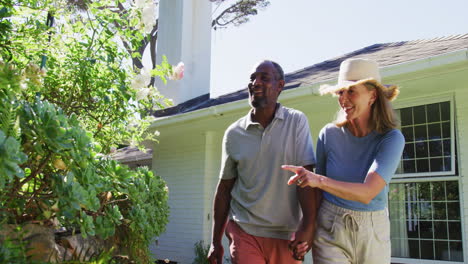 Diversa-Pareja-De-Ancianos-En-Su-Jardín-Mirando-Plantas-Y-Hablando-Bajo-El-Sol.