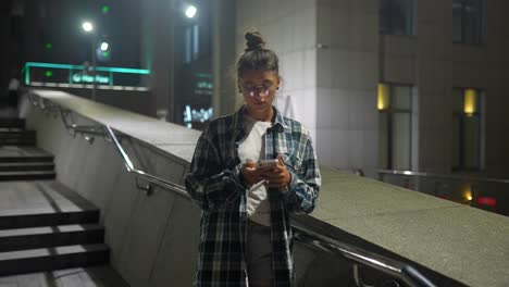 young woman using smartphone at night in city