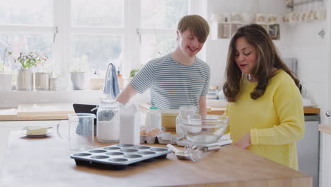 young downs syndrome couple following recipe on digital tablet to bake cake in kitchen at home