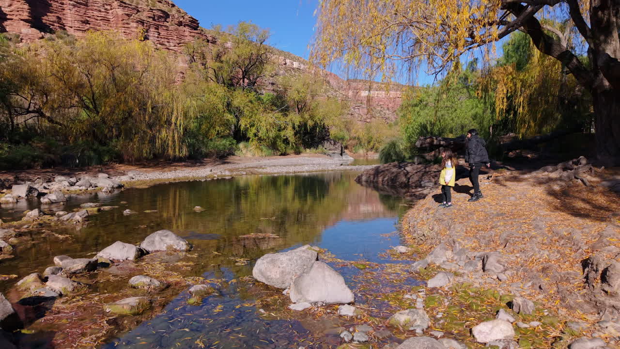 Child and mother skip stones on a small lake framed by vibrant autumn colors and nature