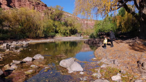 child and mother skip stones on a small lake framed by vibrant autumn colors and nature