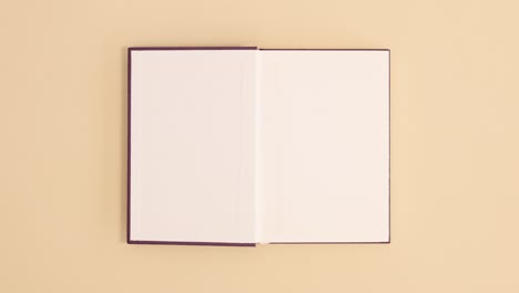 purple hardcover vintage book appear and open with copy space on beige background. stop motion flat lay