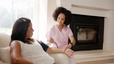 nurse in pink scrubs checking blood pressure of woman sitting on couch