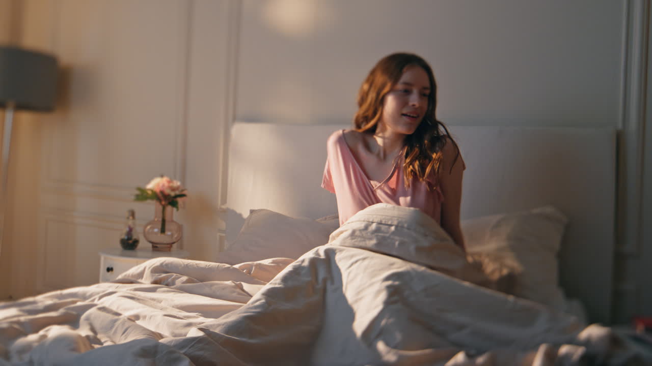 웃는 소녀가 아침 빛에 깨어나 행복한 긍정적 인 여성이 휴대전화를 확인합니다.