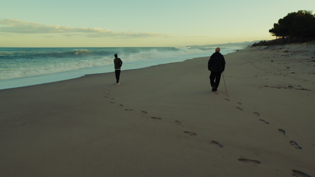 Two Lonely Men in Winter Search for Something on a Deserted Beach at Sunset