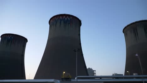 two large cooling towers stand against the twilight sky, illuminated by lights, representing the energy production process at a power facility.