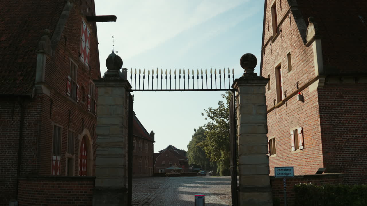 Courtyard entrance of Schloss Raesfeld with historic gate, cobblestone path, and medieval buildings in a bright setting