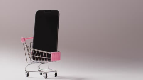 Smartphone-in-shopping-trolley-on-seamless-grey-background