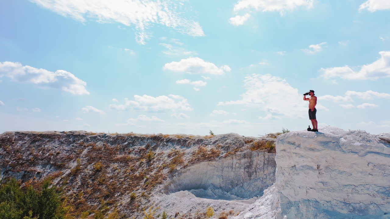 Brutal strong bodybuilder posing outdoor. Photoshoot in a quarry. Outdoor sports concept. Aerial view. Handsome strong man drinks water outdoor. White landscape.