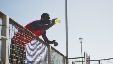 African-american-man-drinking-from-water-bottle-and-taking-break-in-exercise-outdoors