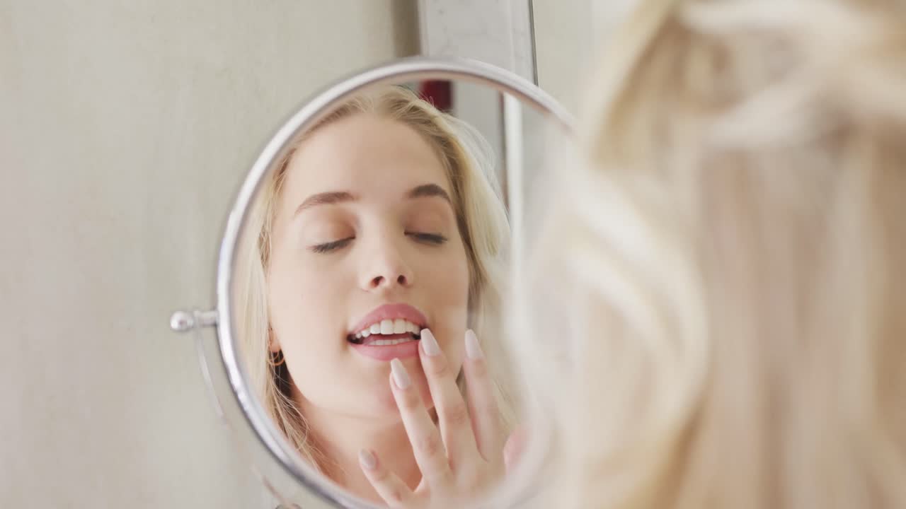 화장실에서 슬로모션으로 화장을 하는 거울 앞에 있는 행복한 백인 플러스 사이즈 여성
