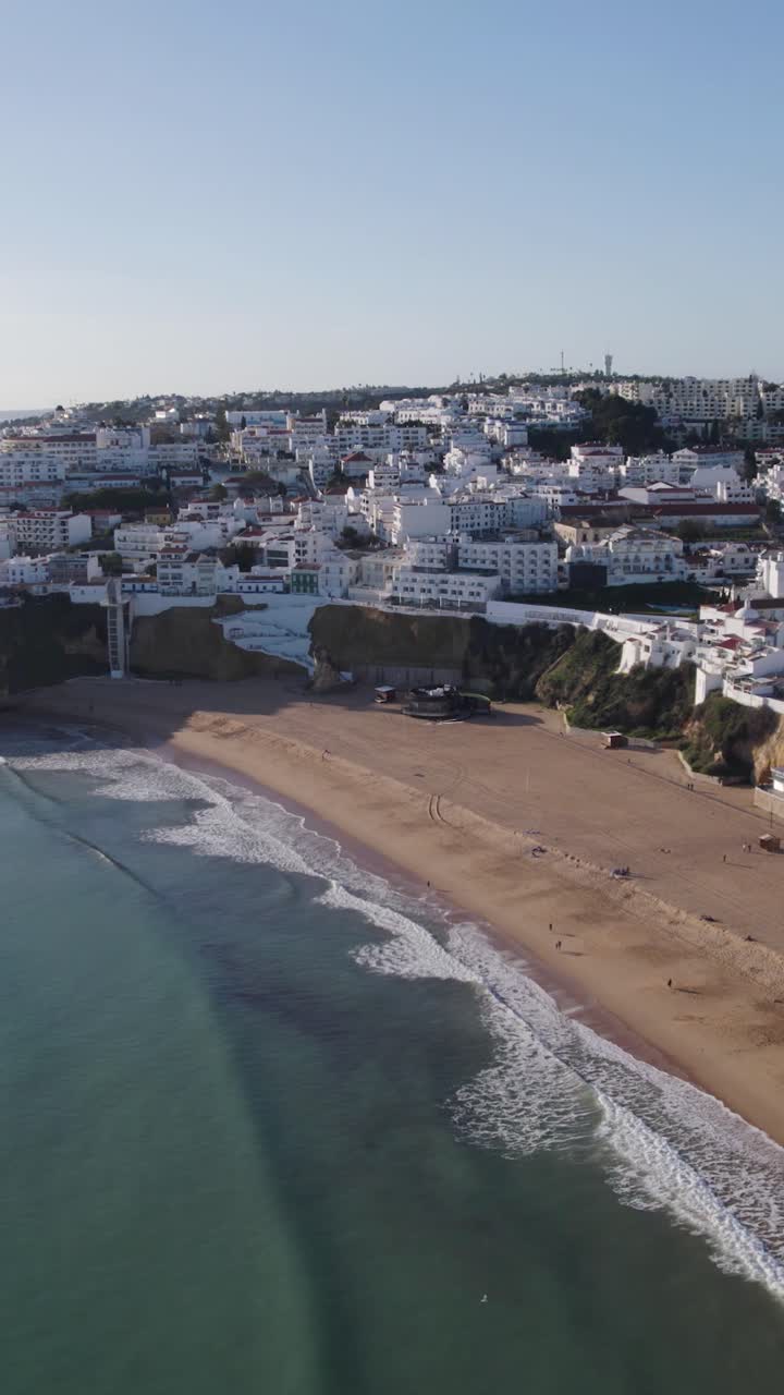 Ripresa aerea verticale di un'ampia spiaggia sabbiosa con onde dolci e condomini bianchi ad Albufeira, Portogallo.