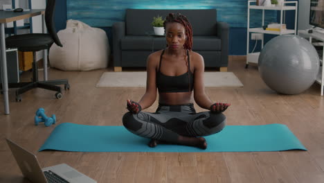 Mujer-Negra-Delgada-Y-Flexible-Sentada-En-Posición-De-Loto-En-El-Mapa-De-Yoga-En-La-Sala-De-Estar