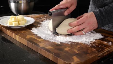 kneading bread dough into a ball on a floured wood cutting board surface