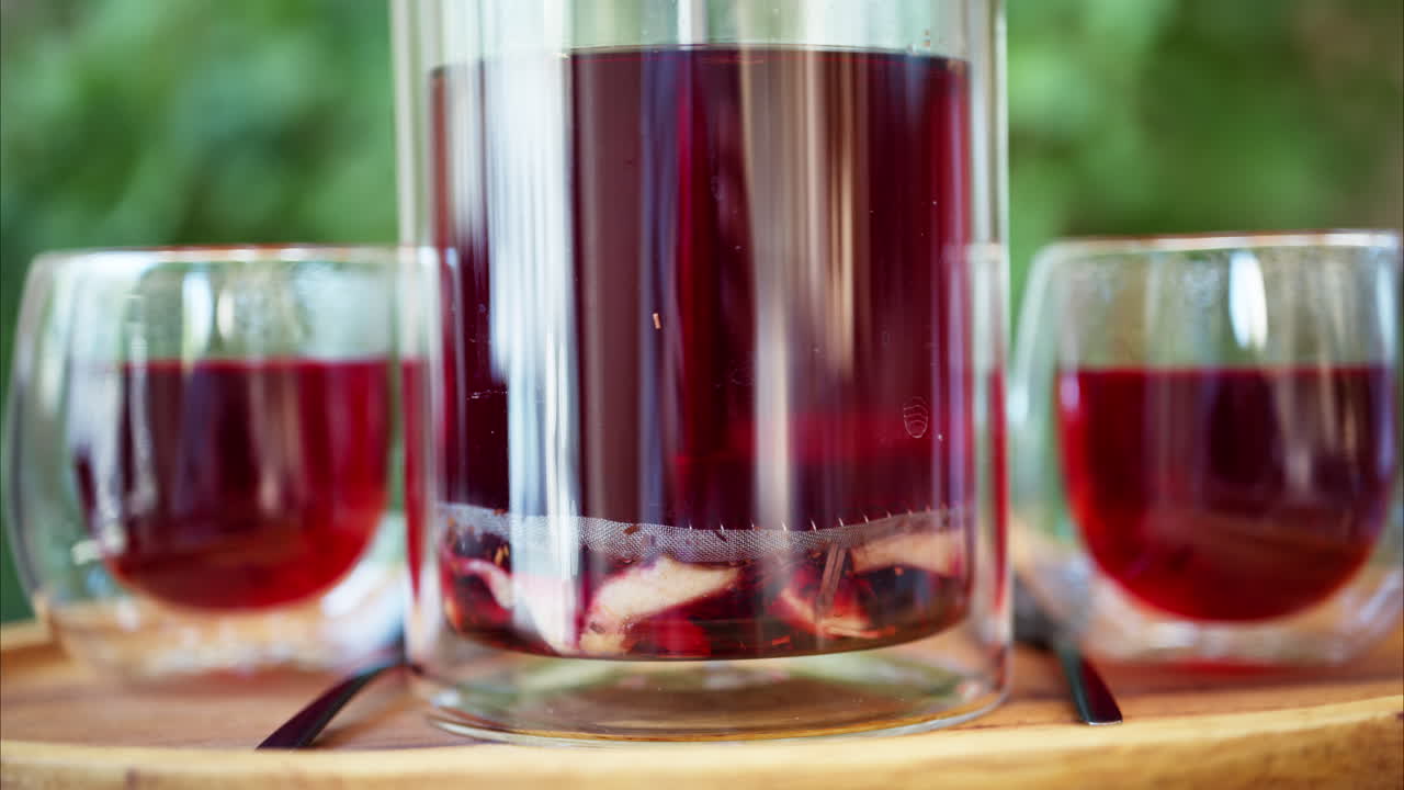 Close up of an infuser teapot with two cups of fruit tea on a table at a terrace