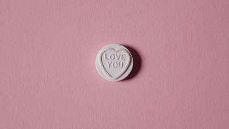 Hand-Picking-Up-Heart-Candy-With-Love-You-Message-On-Pink-Background