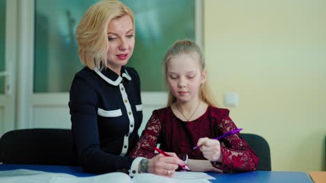 teacher and a schoolgirl in the classroom. female tutor teaches the little girl. elementary school teacher giving a student one to one support in the room.