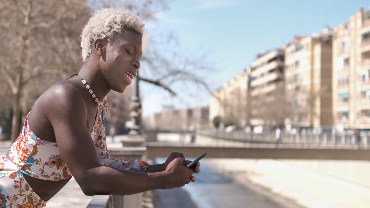 Annoyed black queer man messaging on smartphone on street