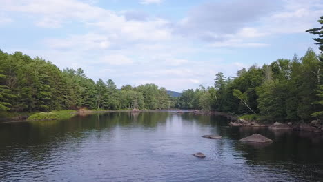 Drone-shot-flying-low-over-a-calm-river-surrounded-by-forest