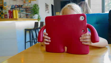 child hiding face behind red tablet case