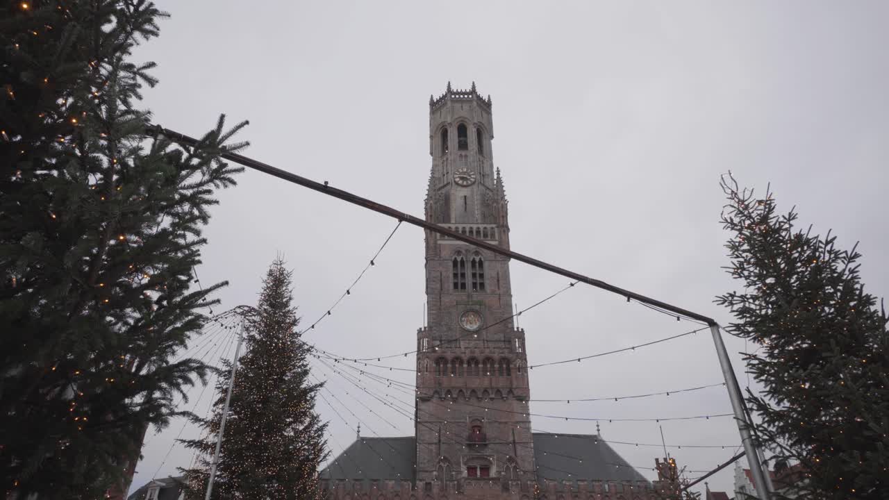 Low wide shot of Christmas trees and belfry on the market square in Bruges, Belgium