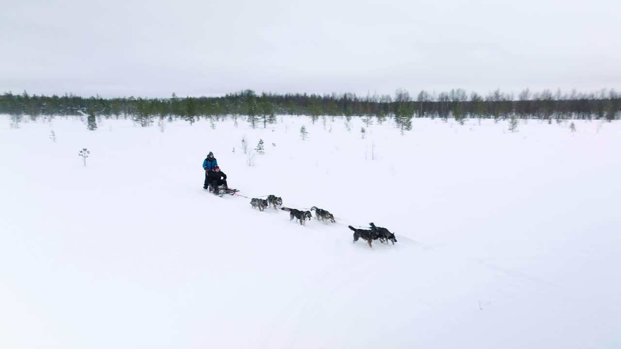 Duas pessoas desfrutando de uma aventura de trenó puxado por huskies no inverno em um campo nevado em Muonio, Lapónia, Finlândia