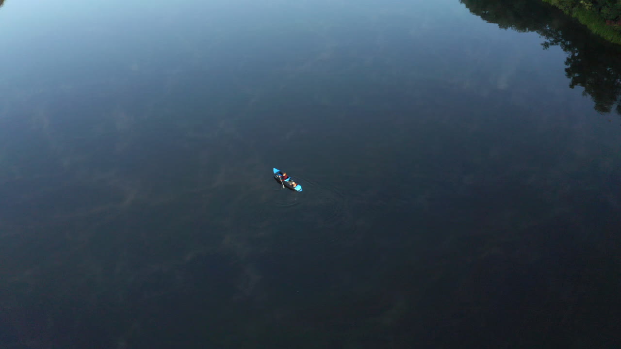 imágenes aéreas de drones de kayak de arriba hacia abajo con personas remando lentamente en un lago tranquilo y relajante con un reflejo impresionante