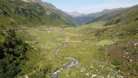 Swiss-National-Park,-Switzerland---Aerial-Drone-View-of-the-Green-Mountain-Valley,-Streaming-River-and-Scenic-Road-during-Summer